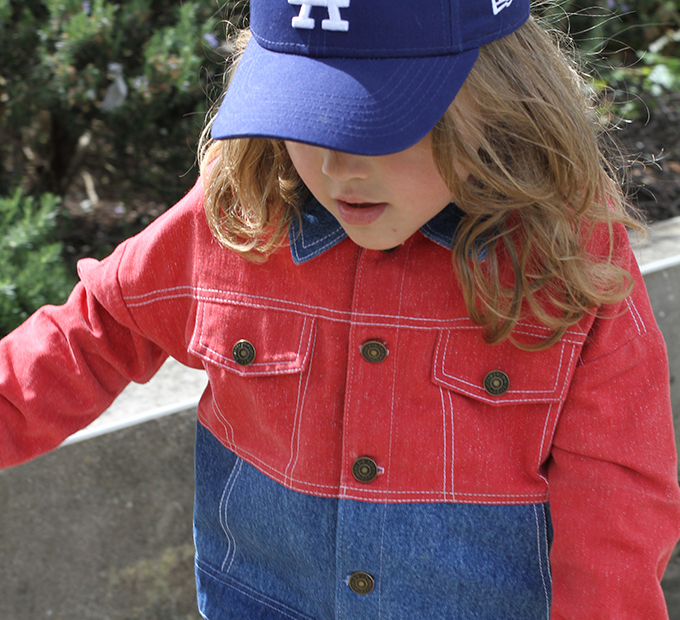 Enfant en veste bicolore rouge et jean, casquette vissée.