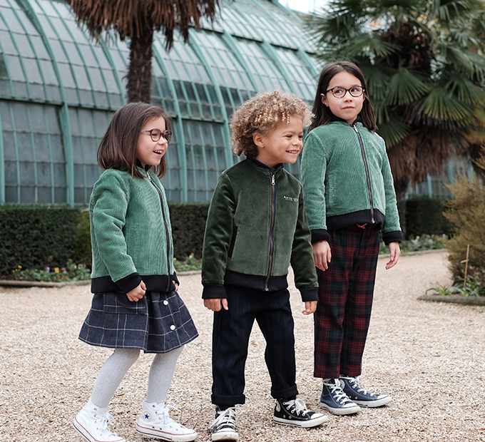 rois enfants en vestes vertes dans un jardin d'hiver.